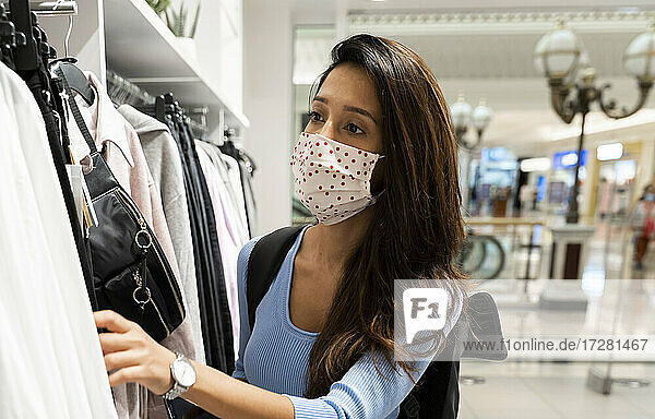 Frau mit Schutzmaske beim Betrachten von Kleidung in einem Einkaufszentrum