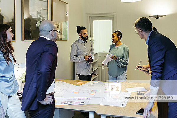 Selbstbewusste Unternehmerin  die am Tisch im Büro mit Kollegen über einen Bauplan diskutiert
