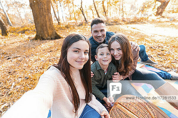 Lächelnde Familie  die ein Selfie macht  während sie im Herbst im Park sitzt