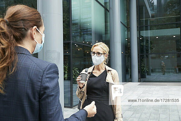 Frauen mit Gesichtsmaske beim Gespräch gegen Bürogebäude