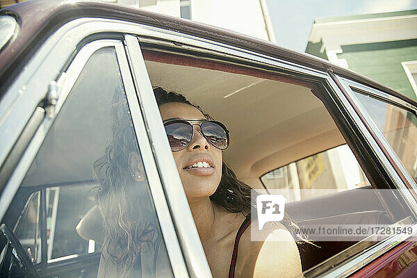 Young woman looking through window while sitting in car on sunny day
