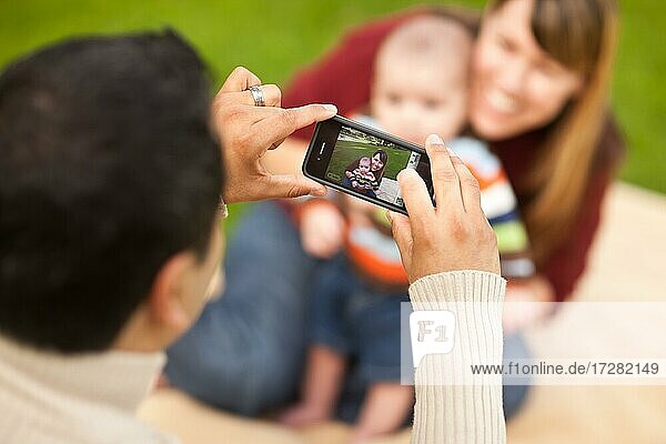Happy mixed-race parents and baby boy taking self portraits at the park