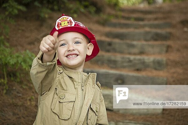 Glücklich adorable Kind Junge mit Feuerwehrmann Hut und Daumen nach oben spielen draußen