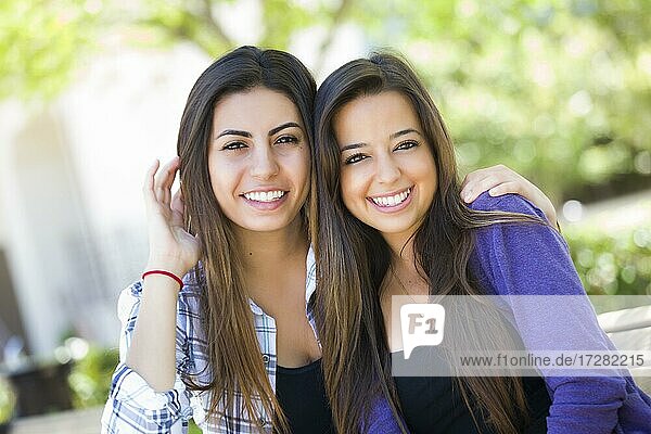 Happy mixed-race young adult female friends portrait outside on bench