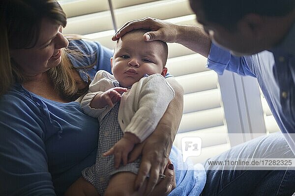 Happy mixed-race couple enjoying their newborn son in the light of the window