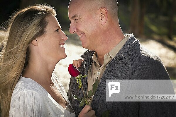 Attraktives junges Paar in Pullover mit einer Rose im Park