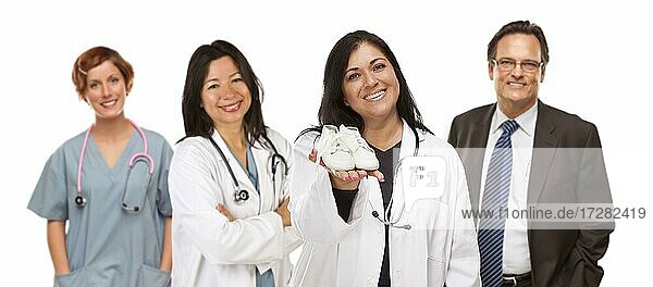 Attractive hispanic female doctor or nurse holding out baby shoes and support staff behind isolated on a white background