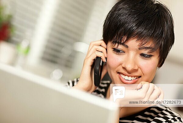 Hübsche lächelnde multiethnische Frau mit Handy und mit ihrem Laptop