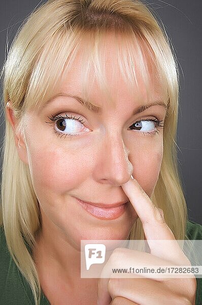 Blonde Frau mit Finger in der Nase vor einem grauen Hintergrund