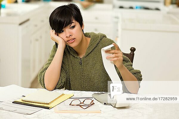 Multi-ethnic young woman agonizing over financial calculations in her kitchen