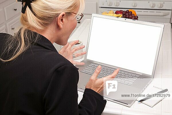 Woman sitting in kitchen using laptop with blank screen. screen can be easily used for your own message or picture using the included clipping path