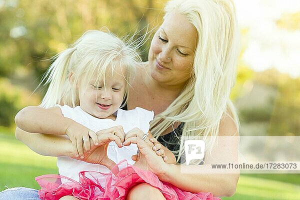 Nettes kleines Mädchen mit Mutter machen Herzform mit Händen im Freien