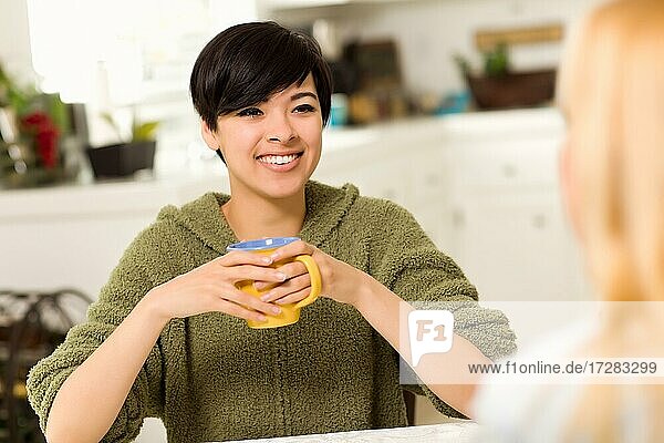 Multi-ethnic young attractive woman socializing with friend in her kitchen