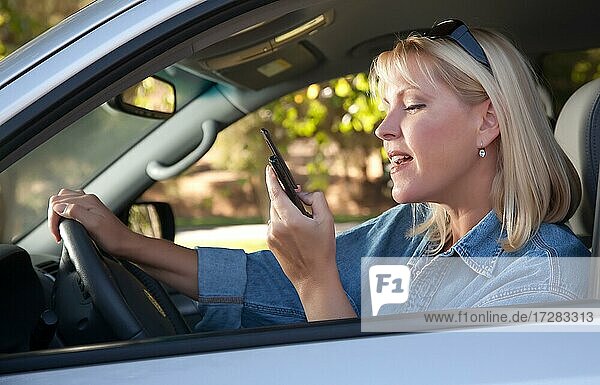Attractive blonde woman text messaging on her cell phone while driving