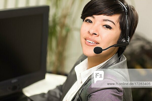 Attraktive junge gemischtrassige Frau lächelt mit Headset in der Nähe ihres Computers in einer Büroumgebung