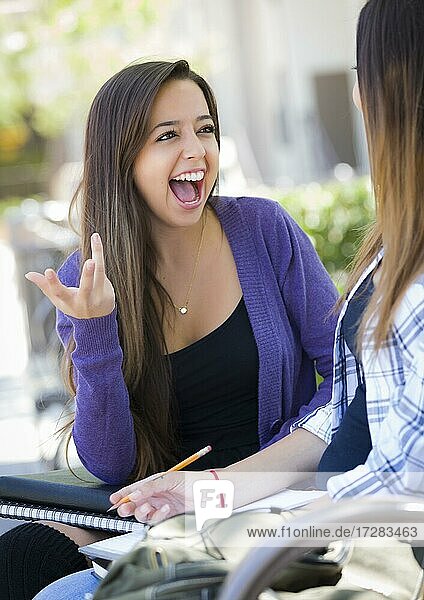 Attraktive ausdrucksstarke junge gemischtrassige Studentin sitzt und spricht mit Freundin draußen auf der Bank