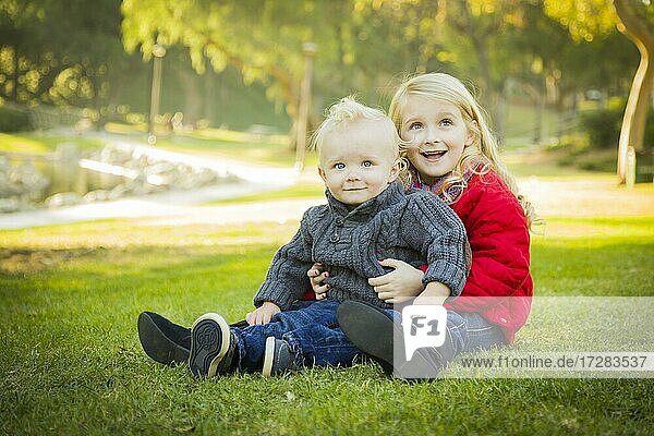 Little girl with her baby brother wearing winter coats outdoors sitting at the park