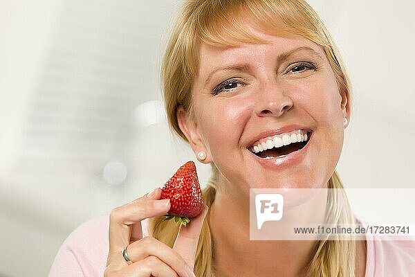 Hübsche lächelnde blonde Frau hält Erdbeere in ihrer Küche