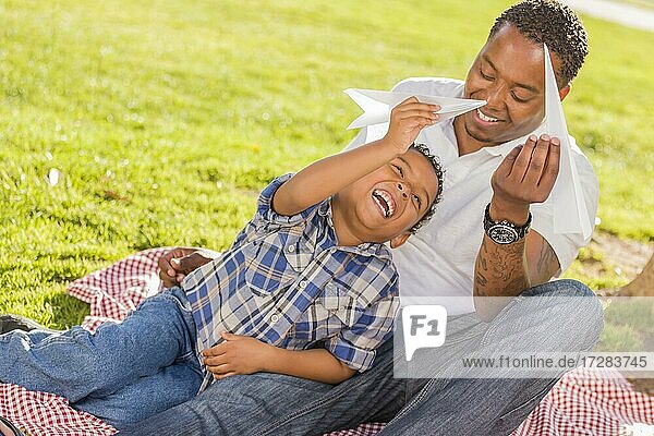 Glücklicher afrikanischer amerikanischer Vater und gemischtrassiger Sohn spielen mit Papierfliegern im Park