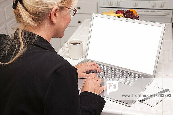 Woman sitting in kitchen using laptop with blank screen. screen can be easily used for your own message or picture using the included clipping path