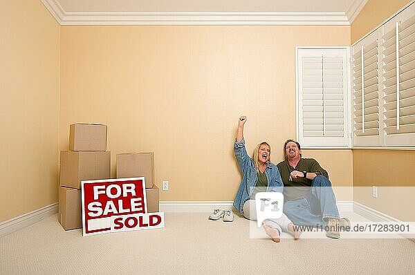 Aufgeregtes Paar entspannt sich auf dem Boden in der Nähe von Kisten und verkauften Immobilienschildern im leeren Raum
