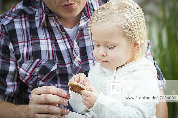 Adorable kleines Mädchen essen einen Keks mit Papa draußen