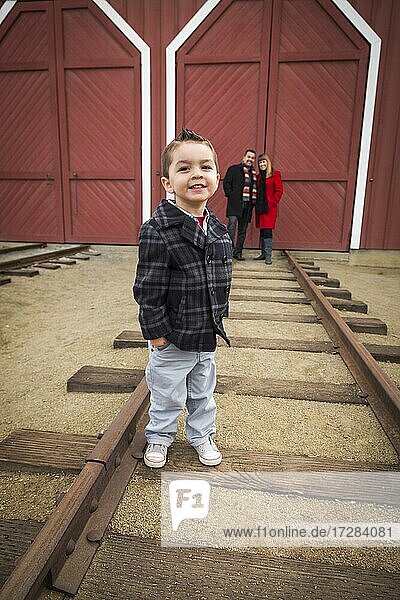 Young adorable mixed-race boy at train depot with parents smiling behind