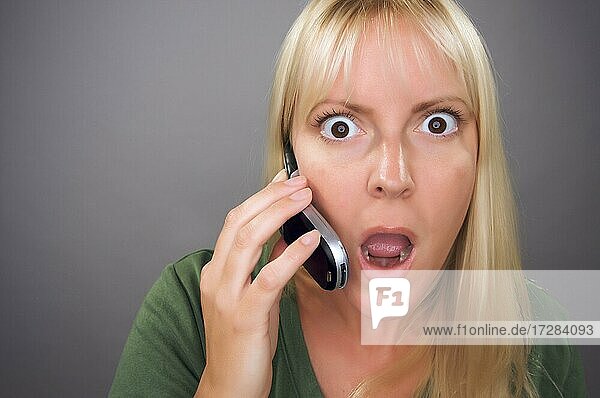 Stunned blond woman using cell phone against a grey background