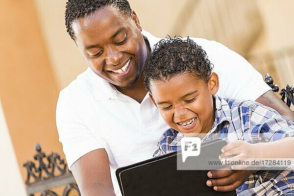 Happy african american father and mixed-race son having fun using touch pad computer tablet outside