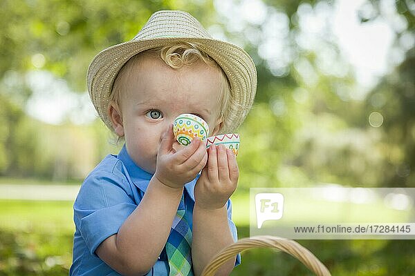Netter kleiner Junge mit Hut genießt seine Ostereier auf Picknickdecke draußen im Park