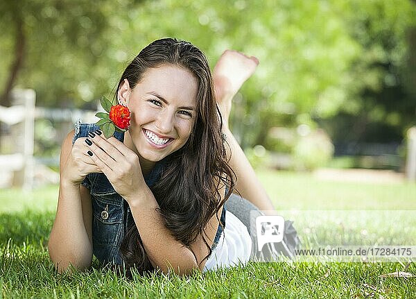 Attractive mixed-race girl portrait laying in grass outdoors with flower