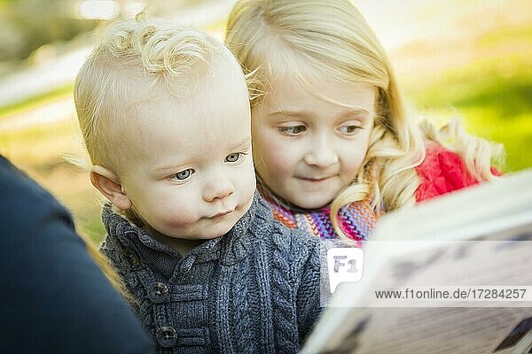 Mutter liest ein Buch zu ihren beiden entzückenden blonden Kinder tragen Wintermäntel im Freien