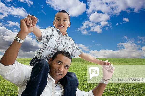 Happy hispanic father and son over grass field  clouds and blue sky