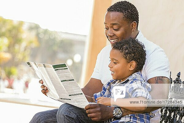 Glücklich afrikanischer amerikanischer Vater und gemischtrassige Sohn mit Spaß lesen Park Broschüre außerhalb