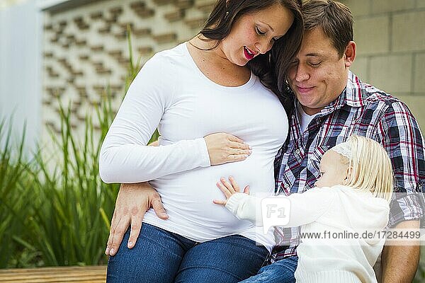 Adorable Baby Mädchen legt ihre Hand auf den Bauch der Mama als Papa schaut auf