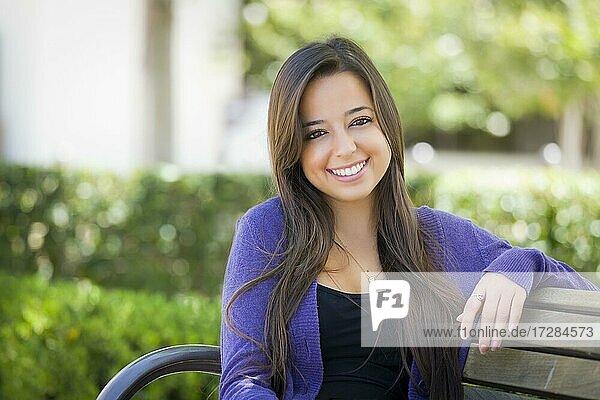 Happy mixed-race female student portrait on school campus bench