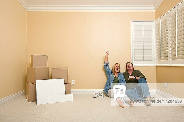 Aufgeregtes Paar entspannt sich auf dem Boden in der Nähe von Kisten und leeren Immobilienschildern in einem leeren Raum