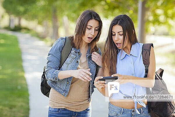 Young adult mixed-race twin sisters sharing cell phone experience outside