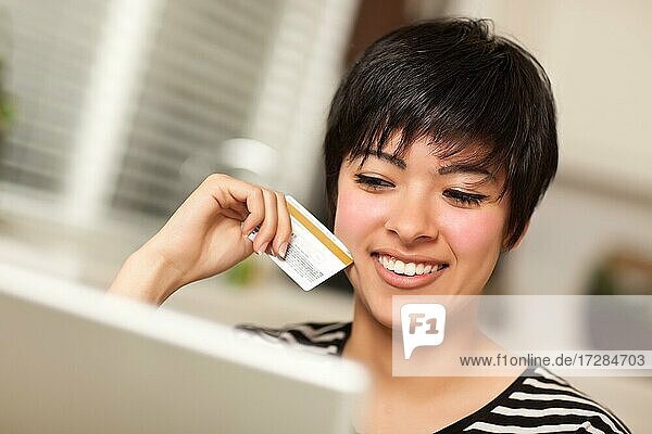 Lächelnde multiethnische Frau hält eine Kreditkarte  während sie einen Laptop benutzt