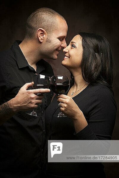 Happy mixed-race couple flirting and holding wine glasses on a dark background