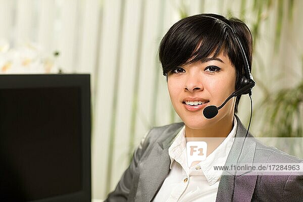 Attraktive junge Frau lächelt und trägt ein Headset in der Nähe ihres Computermonitors