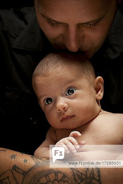 Happy young father holding his mixed-race newborn baby under dramatic lighting