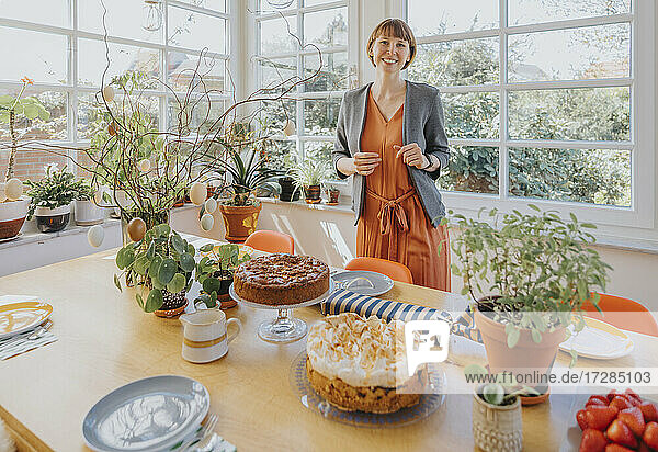 Smiling woman standing by dining table at home during Easter