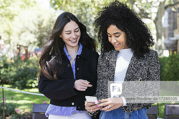 Multiethnische Freundinnen benutzen ihr Smartphone in einem öffentlichen Park