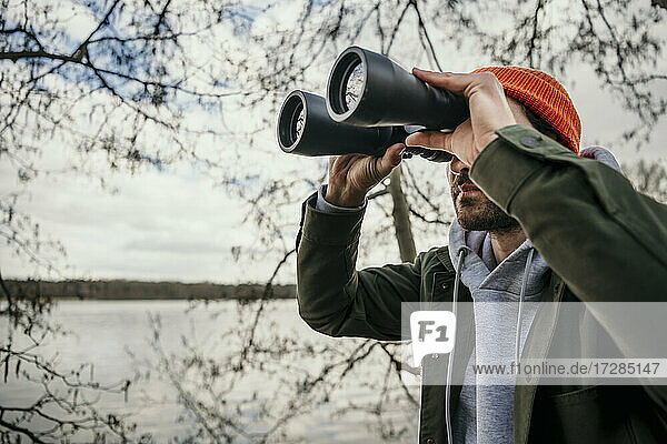 Man looking through binoculars by bare tree