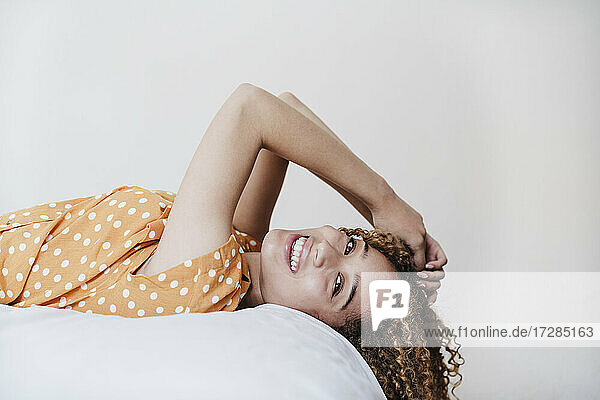 Smiling woman with hand in hair lying on bed at home