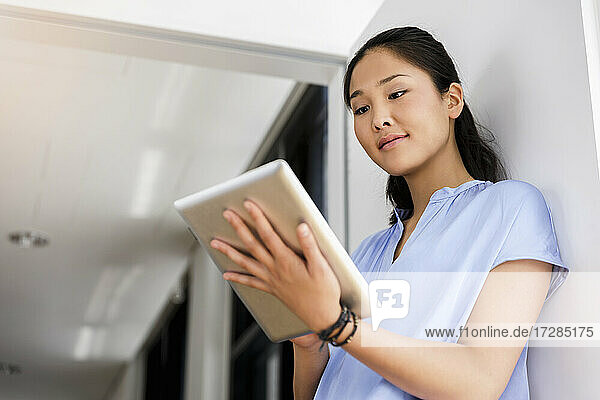 Junge Geschäftsfrau  die im Büro stehend ein digitales Tablet benutzt
