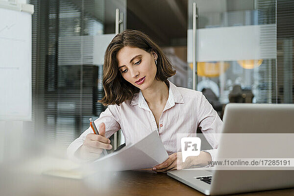 Schöne junge Geschäftsfrau  die ein Dokument liest  während sie am Schreibtisch im Büro sitzt