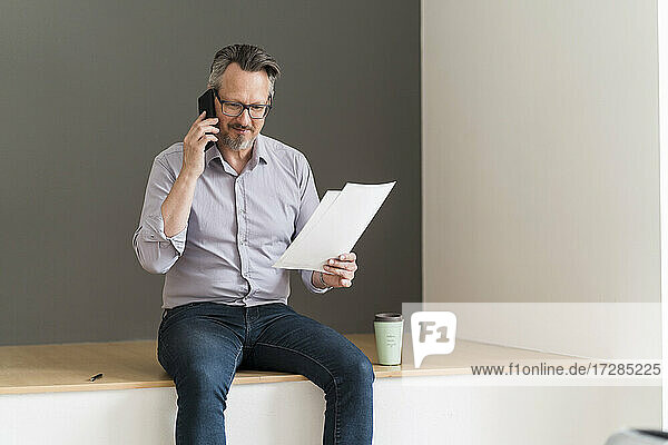 Male entrepreneur with document talking on mobile phone at office