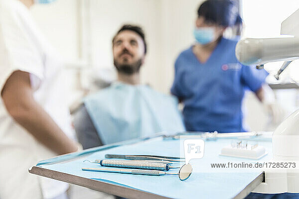 Zahnmedizinische Geräte auf Tablett mit weiblichen Zahnärzten und männlichen Patienten im Hintergrund in einer medizinischen Klinik